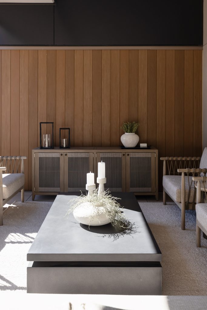 Black rectangular coffee table, white vases with greenery, candles, beige sofas, and a wooden paneled wall with a sideboard — Living with Lolo.
