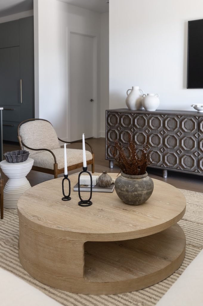 A modern living room includes a round wooden coffee table, two white candlesticks, a ceramic vase with dried plants, and an armchair— Living with Lolo.