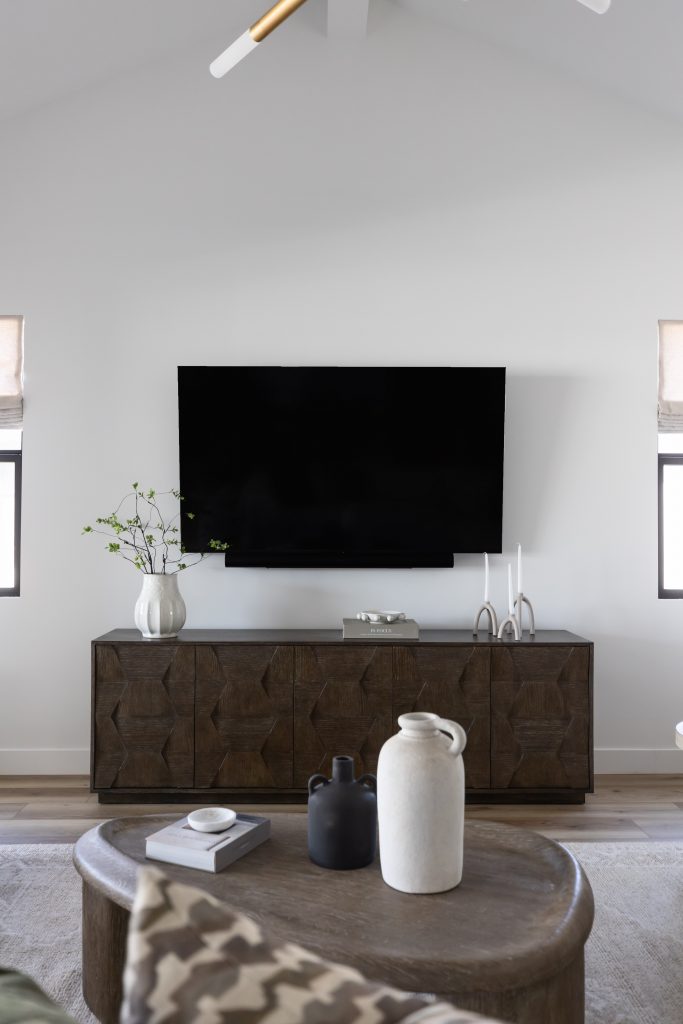 A modern living room features a wall-mounted TV, wooden console, and neutral decor with vases, books, and candles— Living with Lolo.