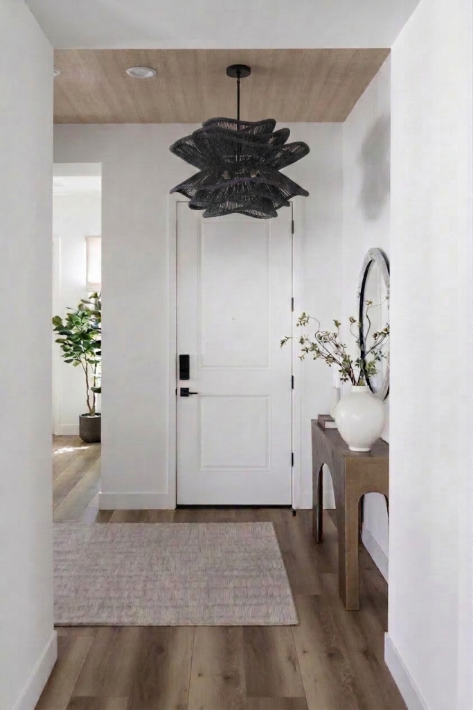A modern entryway with a white door, wood flooring, light rug, console table, vase, mirror, black ceiling light, and potted plant. — Living with Lolo.