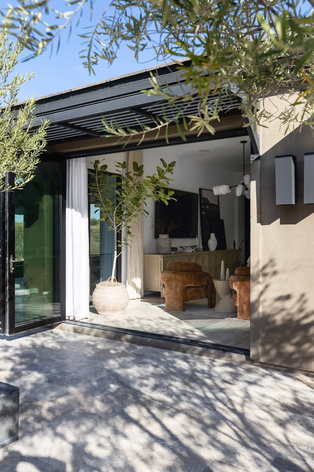 Large glass doors connect a living room with brown armchairs and neutral decor to a stone patio. — Living with Lolo. Premium material and texture detail - Scottsdale interior design trends 2026 Living with Lolo