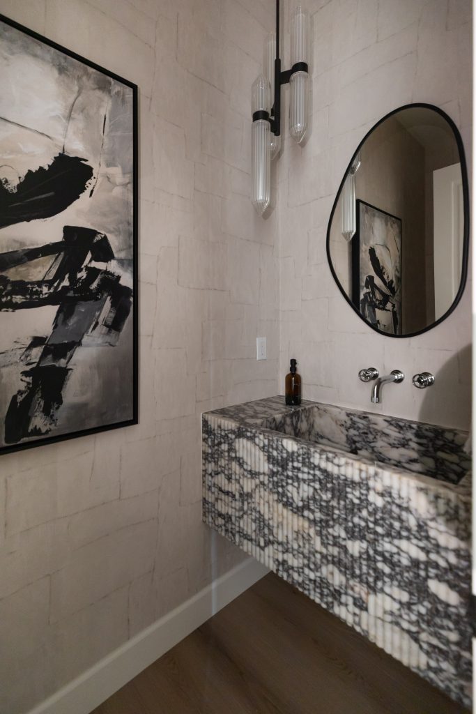 Modern bathroom with a black and white marble sink, oval mirror, wall-mounted faucet, abstract art, and pendant light on beige textured walls—Living with Lolo.