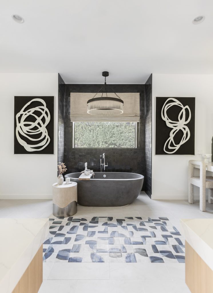 A bathroom with a black freestanding tub, abstract wall art, geometric floor tiles, and a large window covered by a neutral shade. — Living with Lolo.