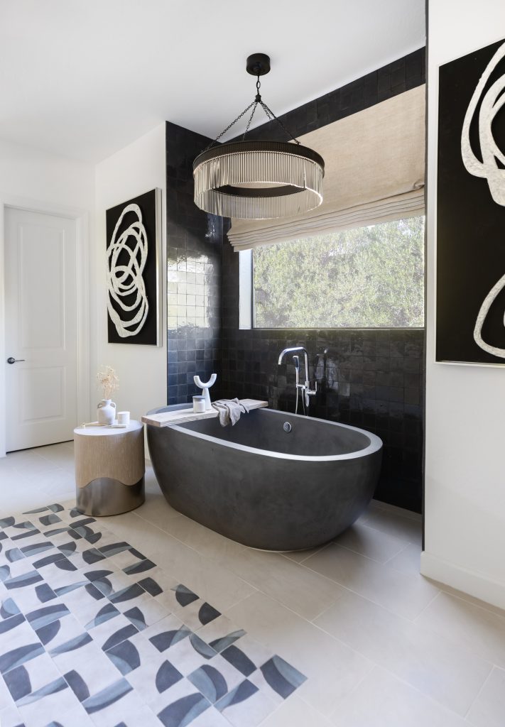 Modern bathroom featuring a matte black tub, abstract wall art, geometric floor tiles, a round side table, and a large window overlooking trees—Living with Lolo.