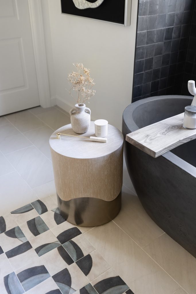 A bathroom features a black bathtub, a round side table with a vase and candle, and patterned floor tiles. — Living with Lolo.