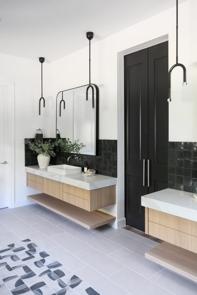 Modern bathroom featuring floating wood vanities, black tile backsplash, large mirrors, pendant lights, a dark door, and a decorative plant on the counter—Living with Lolo.