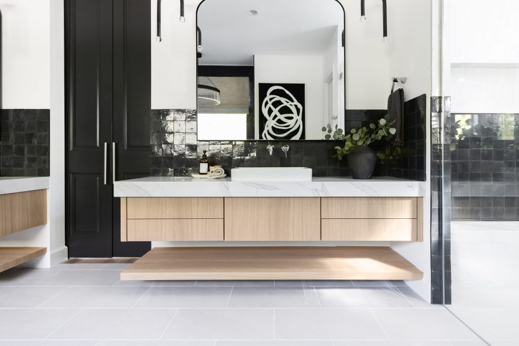 A bathroom with a floating wood vanity, rectangular sink, black tile backsplash, large mirror, a small plant, and abstract wall art on the wall. — Living with Lolo.