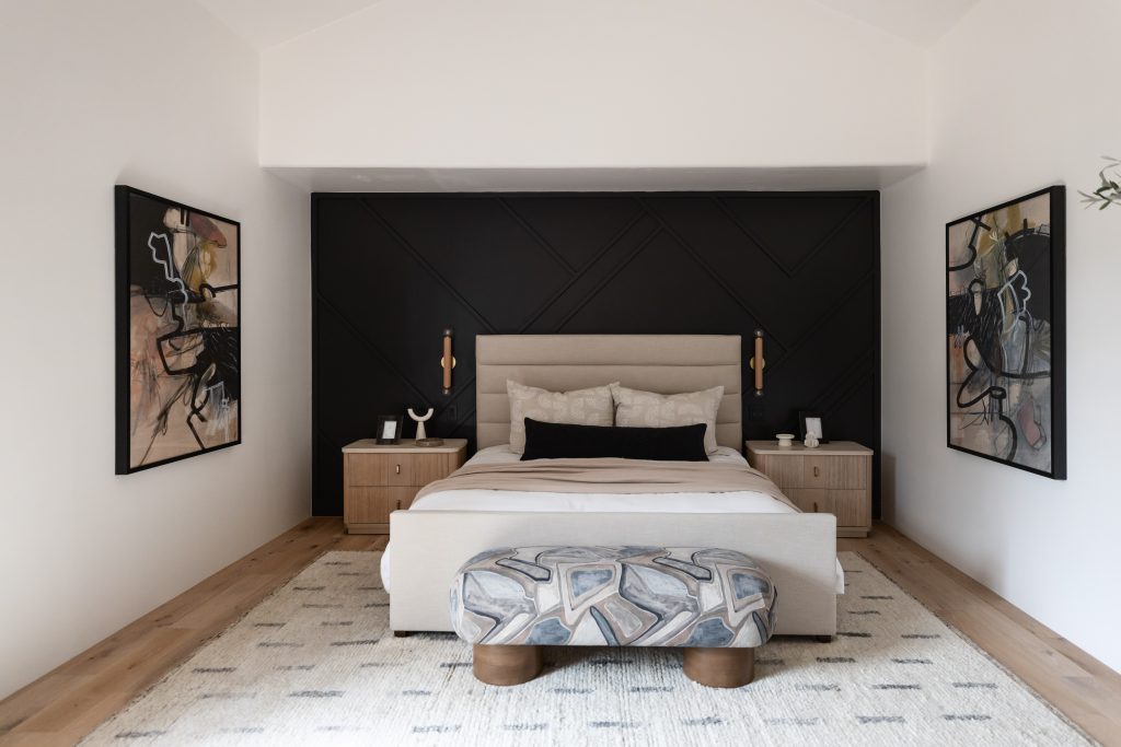 Modern bedroom featuring a beige bed, patterned bench, black accent wall, two nightstands, and abstract artwork on each side of the bed—Living with Lolo.