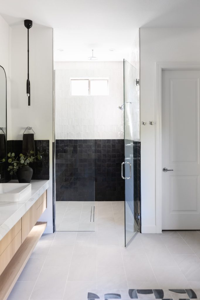 Modern bathroom featuring a glass shower enclosure, black and white tiled walls, a floating vanity with dual sinks, and a small window above the shower—Living with Lolo.