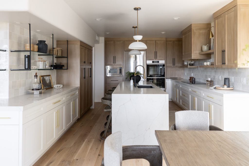 Modern kitchen featuring light wood cabinets, white countertops, an island with barstools, built-in appliances, pendant lights, and a dining table with chairs in the foreground—Living with Lolo.