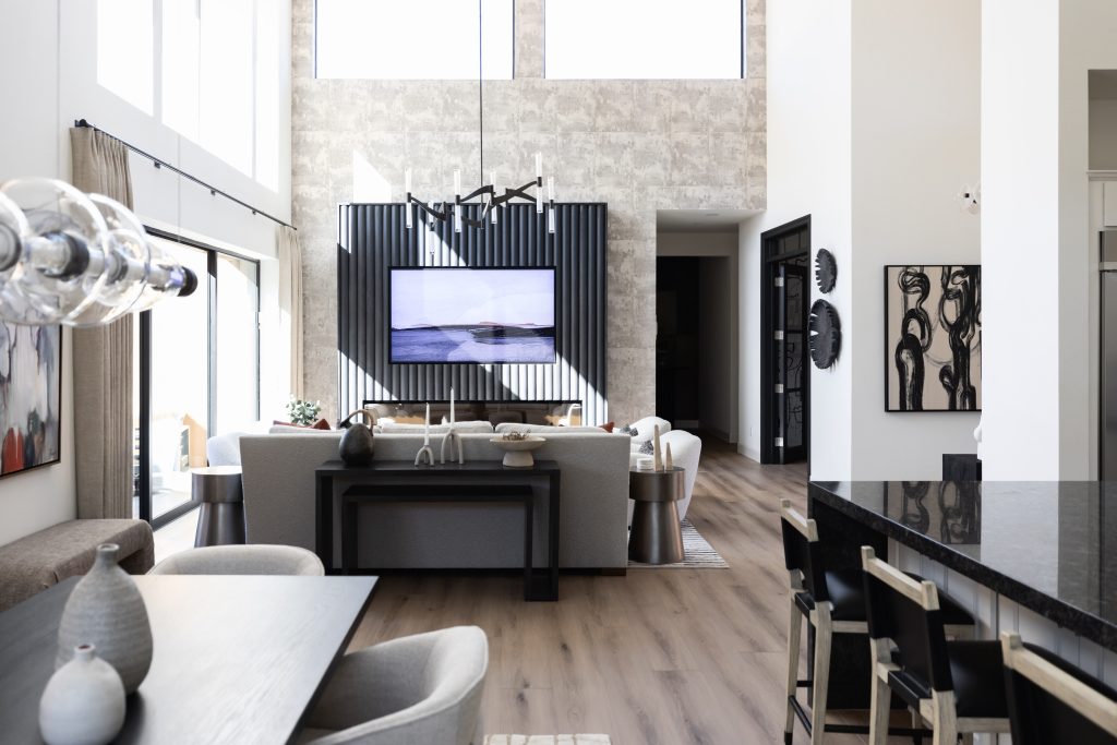 Modern living space featuring high ceilings, large windows, neutral decor, a mounted TV, dining area, and a kitchen island with barstools. Light wood floors and contemporary furnishings are visible — Living with Lolo.