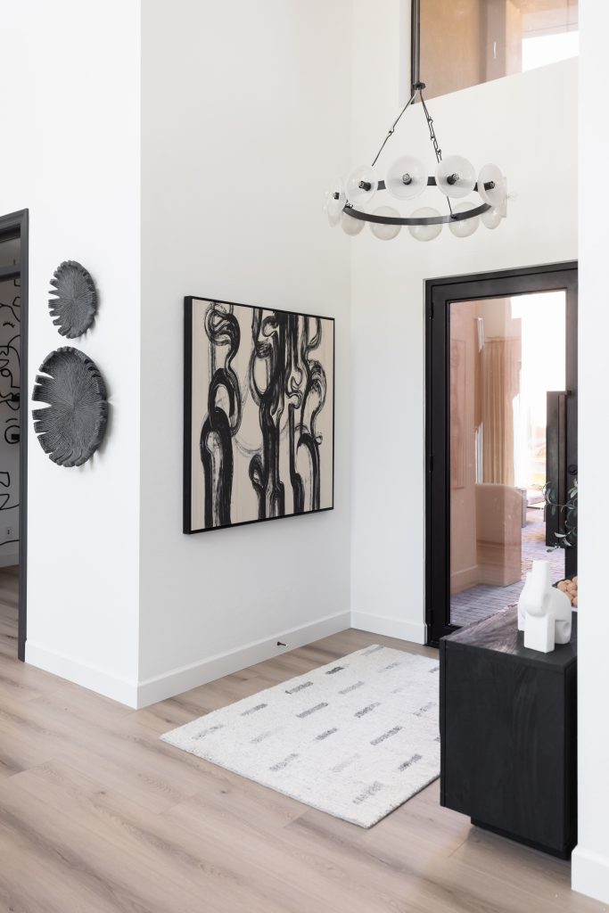 Modern entryway with light wood floors, a white rug, abstract black and white artwork, round wall decor, a circular chandelier, and a glass door leading outside. — Living with Lolo.