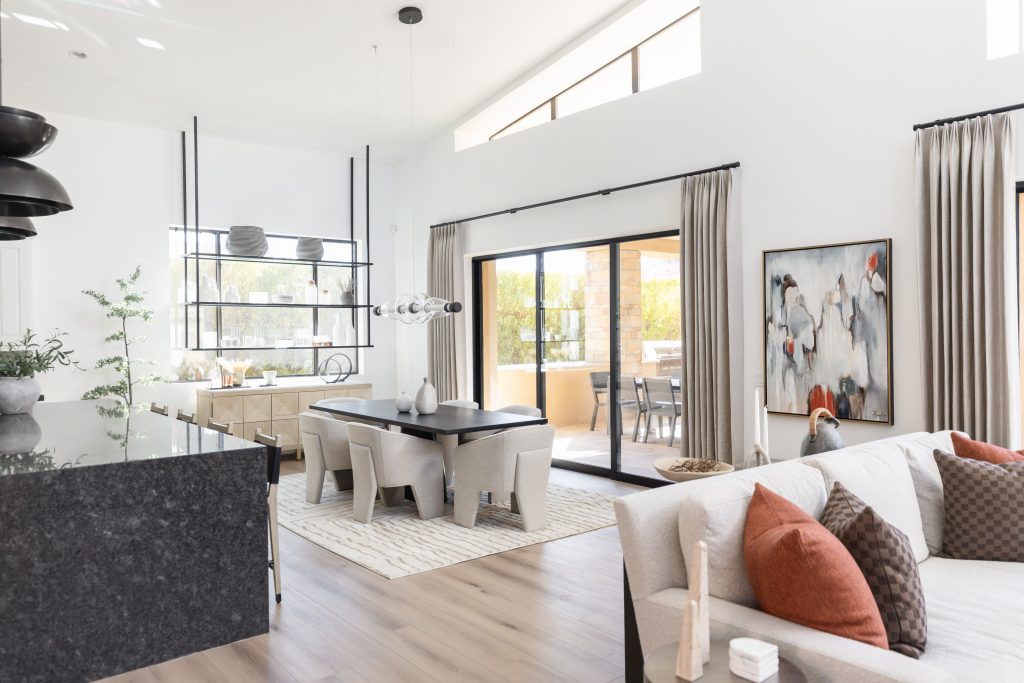 Modern open-plan living and dining area featuring neutral colors, large windows, abstract wall art, a black dining table, and sliding glass doors that open to an outdoor patio. — Living with Lolo.