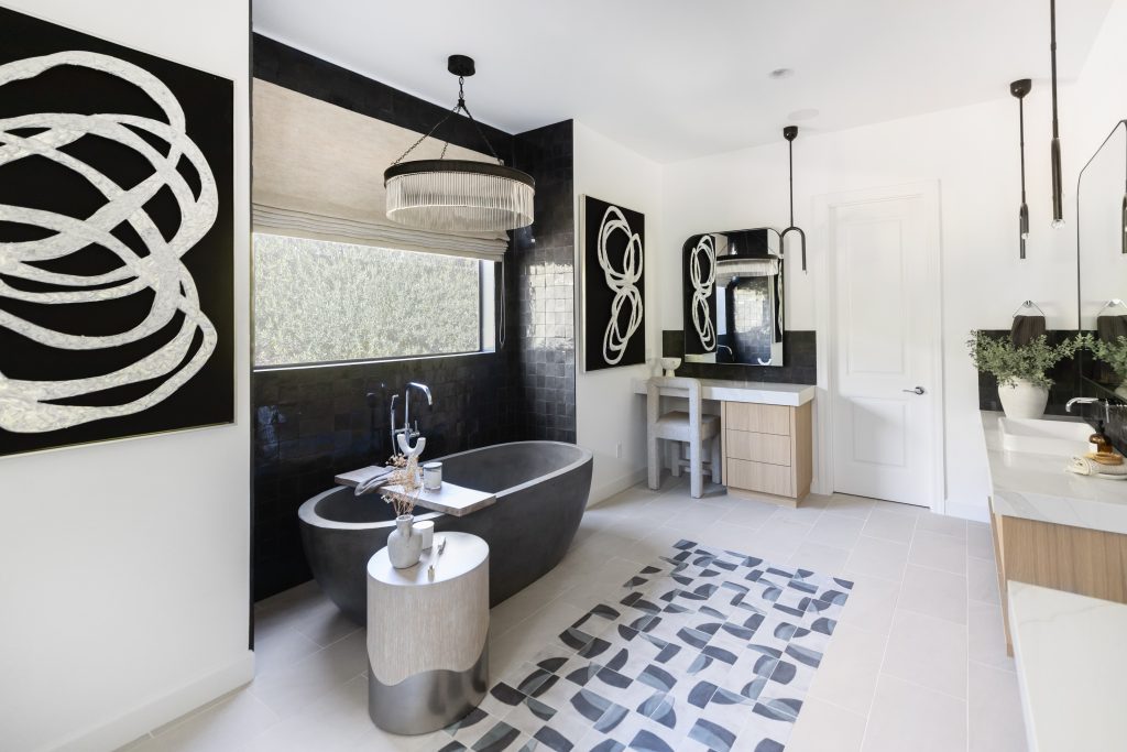 Modern bathroom with a black freestanding tub, geometric rug, large window, abstract wall art, pendant lights, and a double vanity with plants—Living with Lolo.