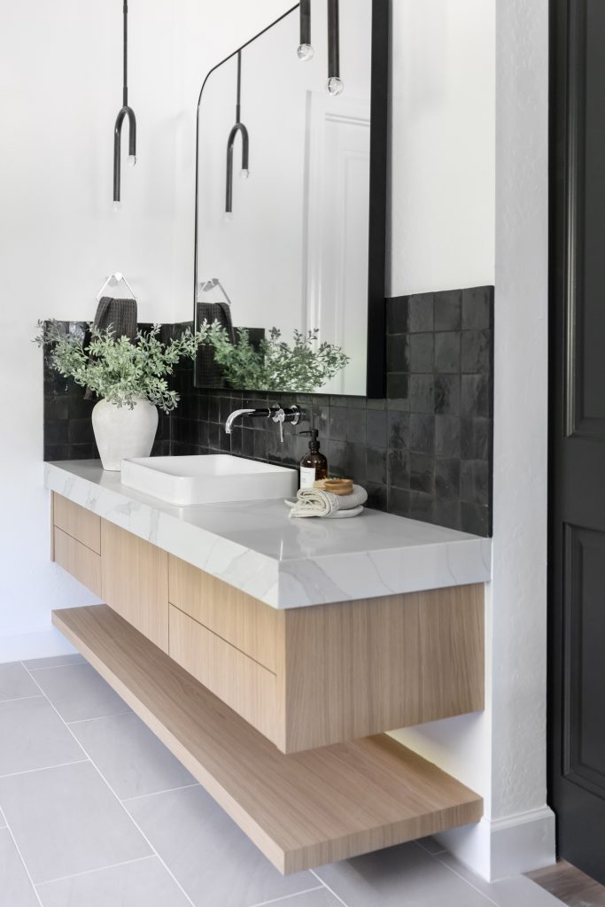 Modern bathroom featuring a floating wood vanity, white sink, marble countertop, large mirror, black tile backsplash, and a decorative plant—Living with Lolo.