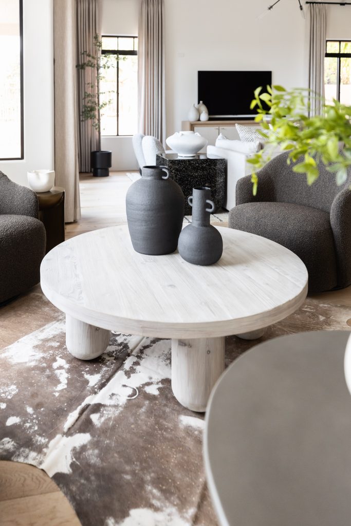 A living room with a round white coffee table, two dark vases, brown armchairs, a TV on a console, and large windows with beige curtains. — Living with Lolo.