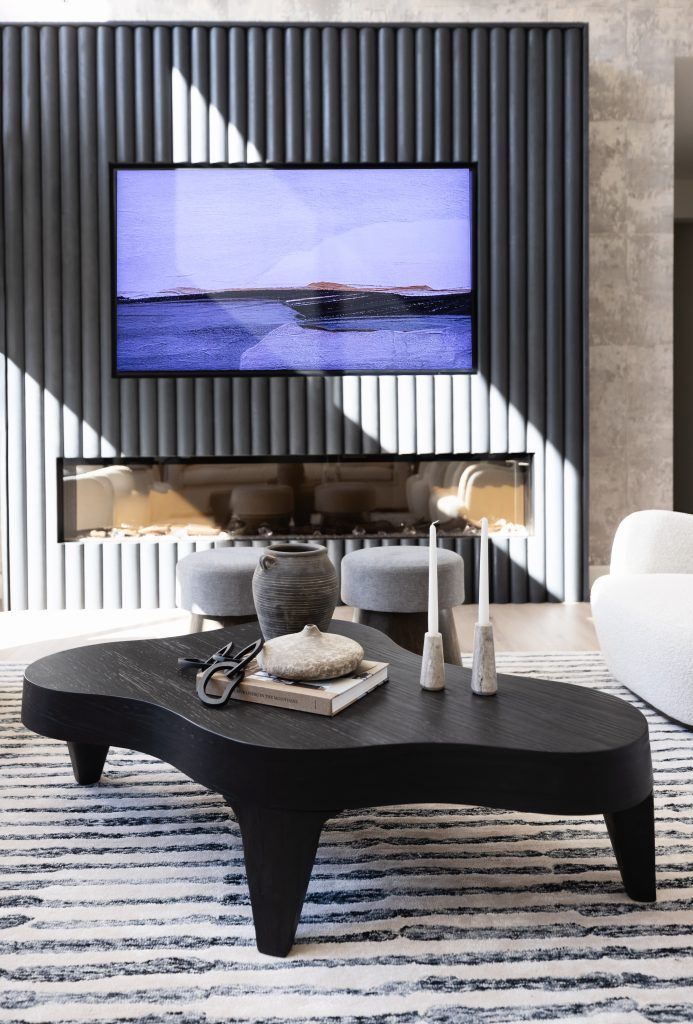 A modern living room with a dark wood coffee table, decorative objects, a striped rug, a wall-mounted TV displaying artwork, and a textured accent wall. — Living with Lolo.