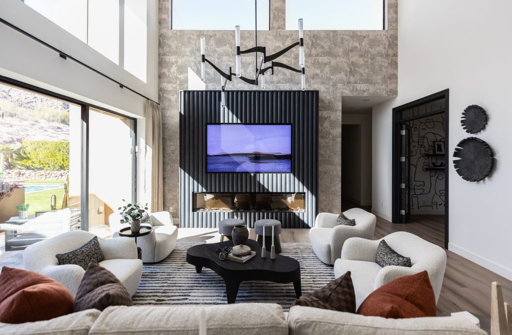 Modern living room featuring white armchairs, a black coffee table, a wall-mounted TV, large windows, and a patterned accent wall. Decorative items are placed on the tables and walls—Living with Lolo.
