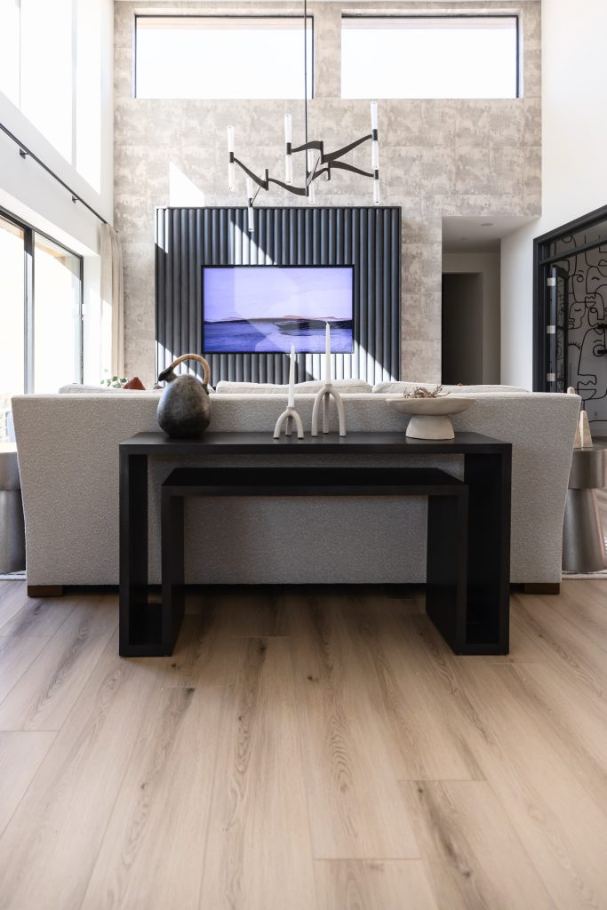 Modern living room featuring a light wood floor, gray sofa, black console table, wall-mounted TV, decorative objects, and large windows bringing in natural light—Living with Lolo.